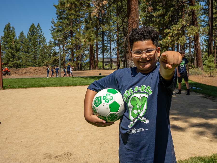 Youth holding a soccer ball and pointing at the camera. 