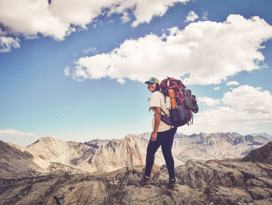 Autumn Harry hikes atop a mountain peak wearing a backpacking pack.