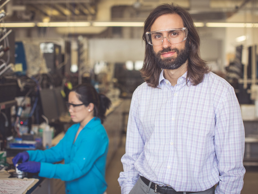 Christopher Barile stands in his lab while a postdoctoral fellow works at the lab bench behind him.