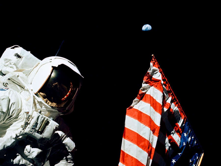 Astronaut and flag in the foreground with Earth in the background far away.