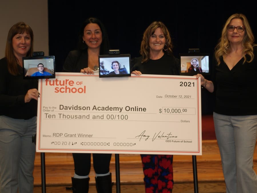 Future of School and Davidson Academy administrators holding onto a large check for $10,000 along with three students joining virtually on tablets attached to on mobile robots