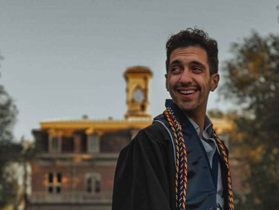 Benjamin Engel stands in front of the University of Nevada, Reno's Morrill Hall building in his graduation robe.