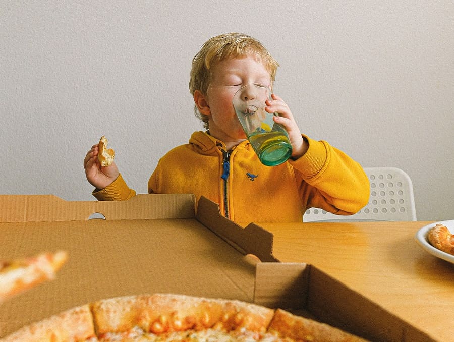 A child eating pizza and drinking something from a glass