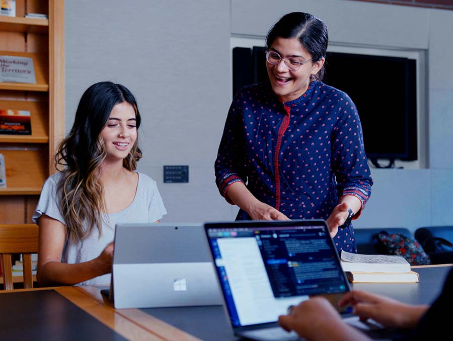 A university student looks at a computer with faculty member Paromita Pain talking to her in the Reynolds School reading room.