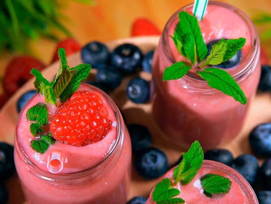 Three glass canning jars filled with raspberry smoothies topped with mint leaves, raspberries and blueberries.