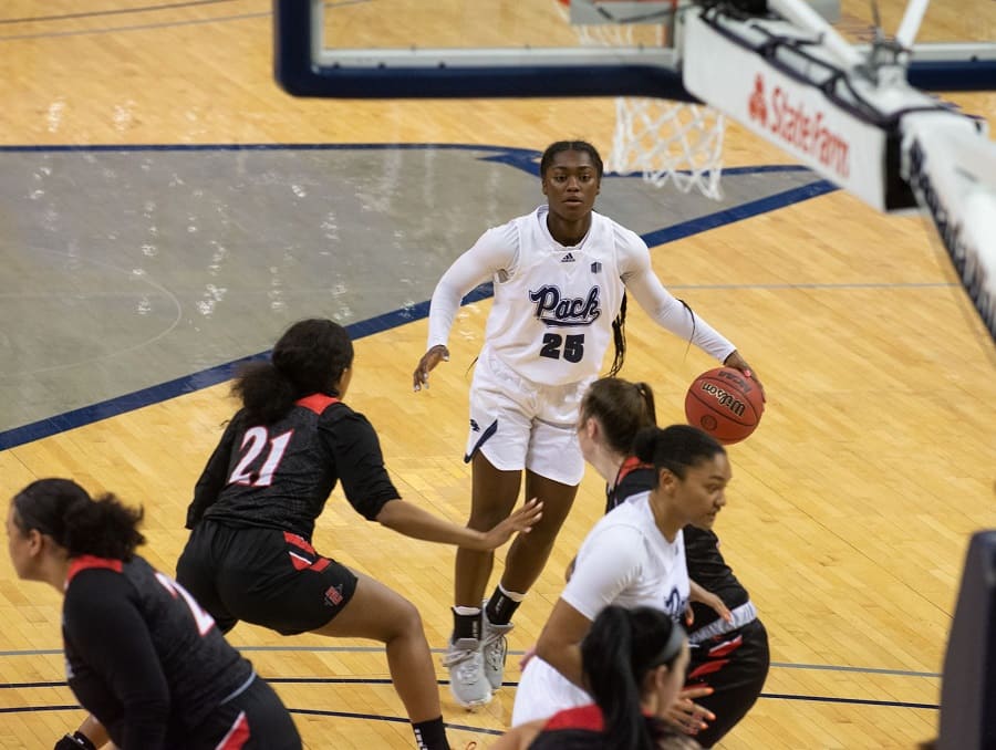 The UNR Women's Basketball team on the court during a game, a Wolf Pack player has the ball