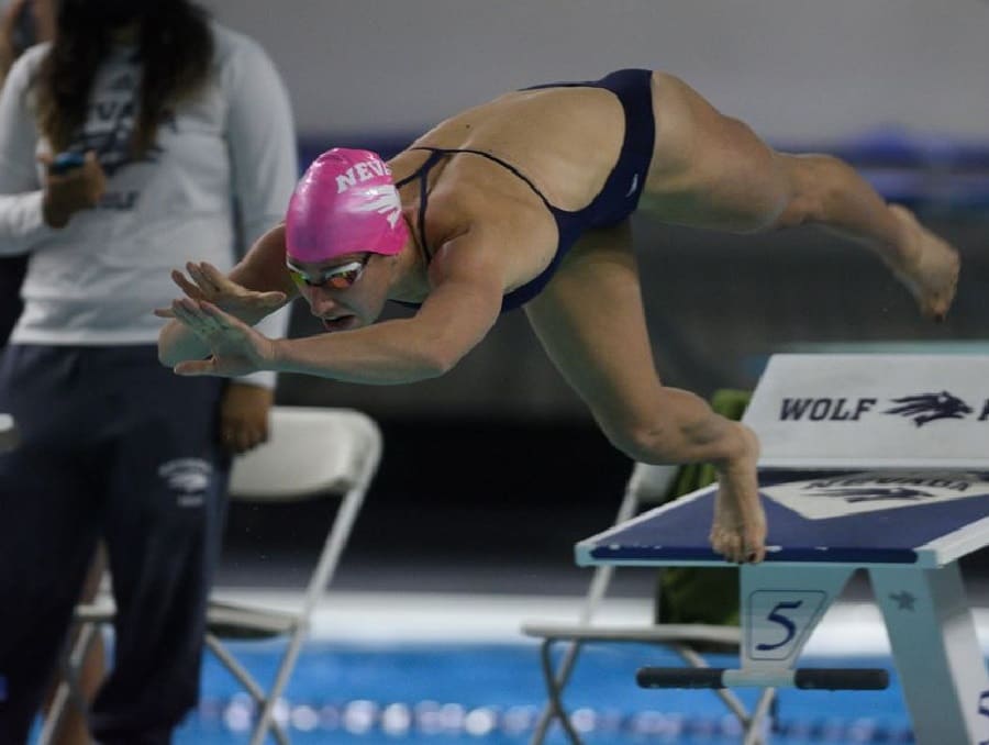 Swimmer on Nevada Swim Team jumping from the platform into the water at a meet