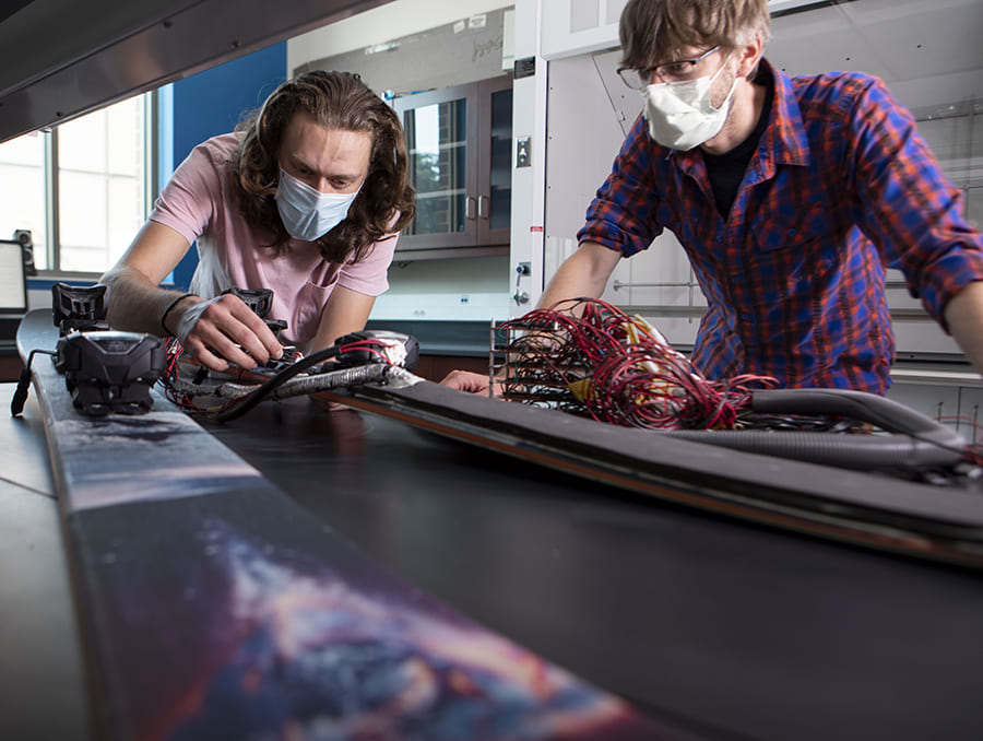 Professor and student working on skis with several electrical cords running from them