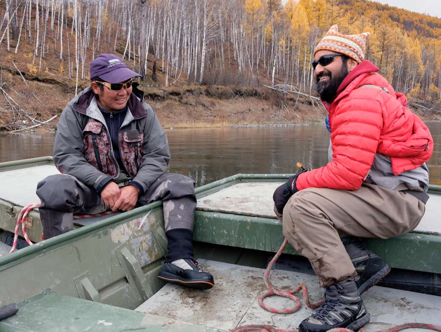 Sudeep Chandra, wearing a red coat, sits in a boat with Ganzorig Batsaikhan, who is wearing a purple hat.