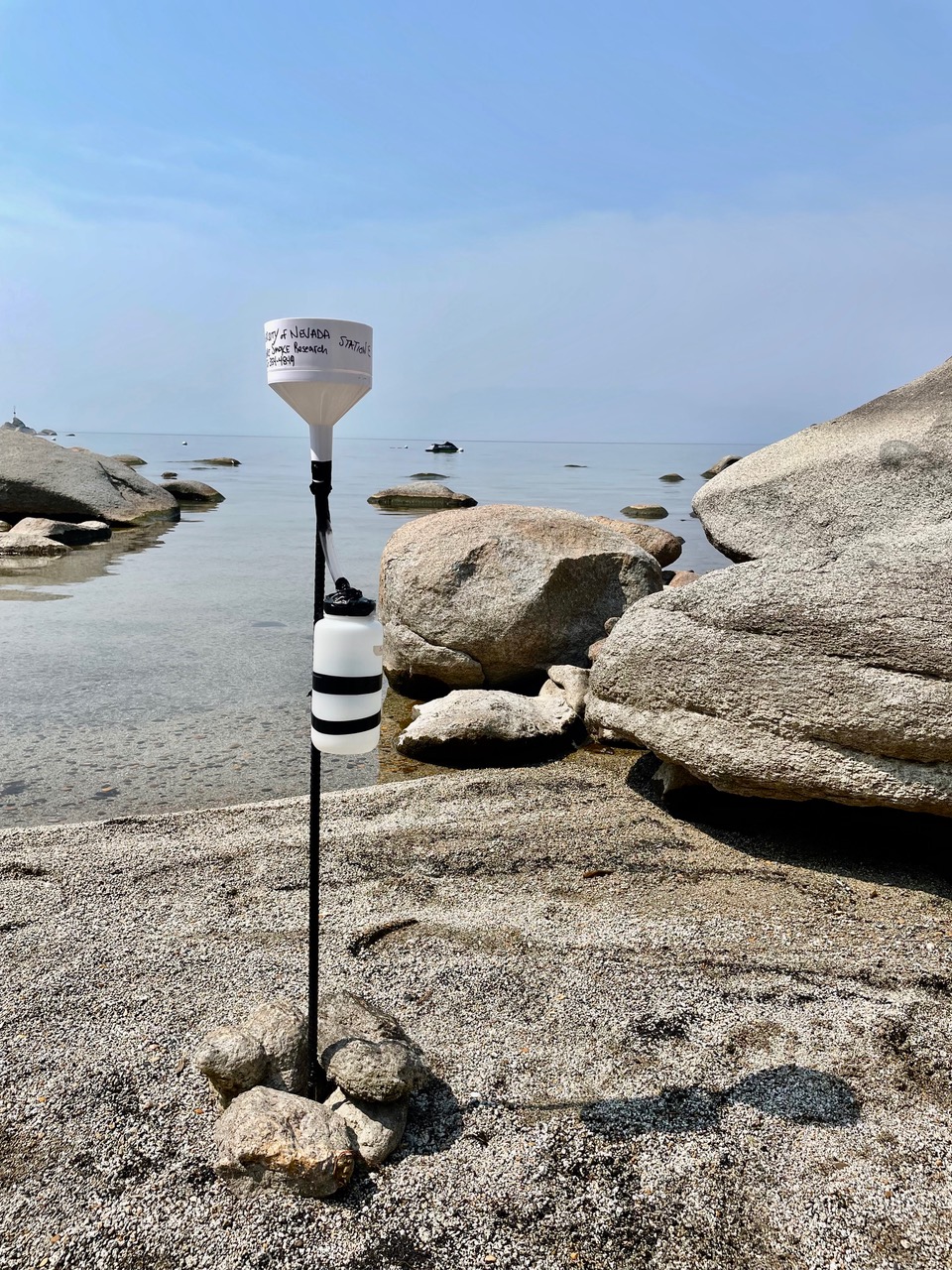 A white bucket secured to the top of a pole is stuck in the sand on Lake Tahoe's shoreline.