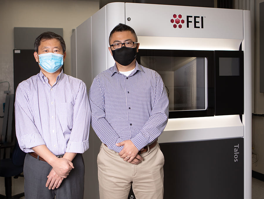 Two professors in masks standing in front of electron microscope