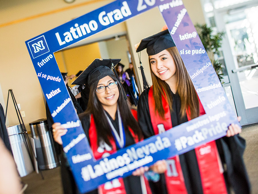 Two students at graduation holding blue picture frame that says "latino grad"