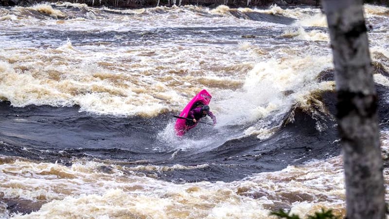 Brooke Hess kayaking a river rapid in a pink kayak.