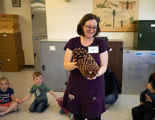 Cynthia Scholl shows a giant pine cone to a group of children.