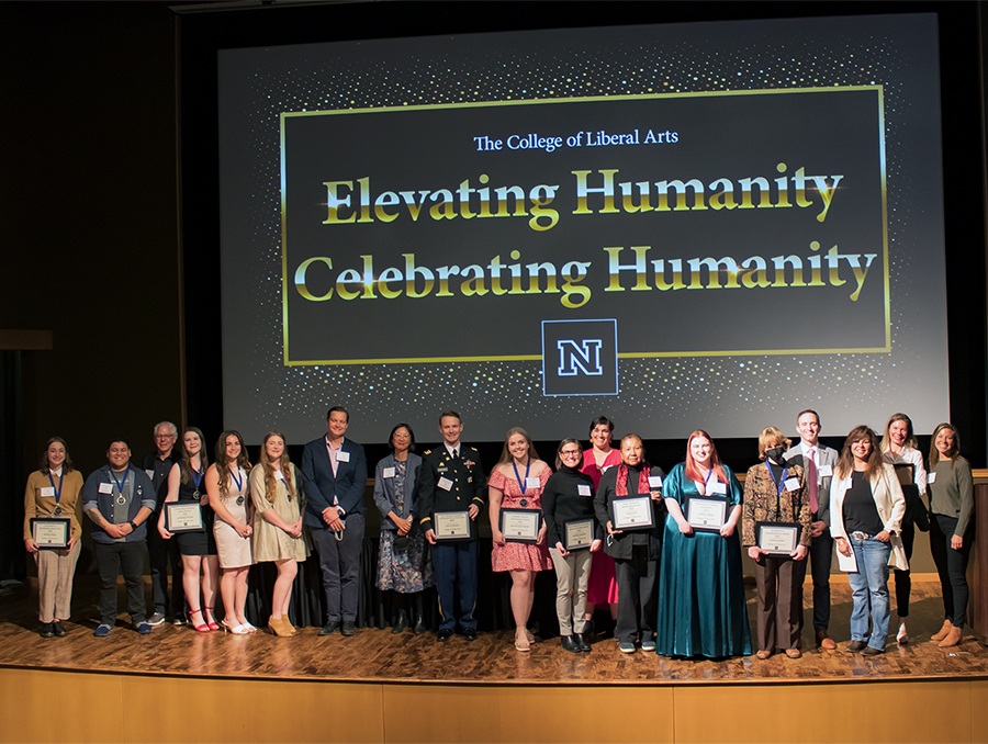 Group of award winners stand on stage during ceremony while holding up awards