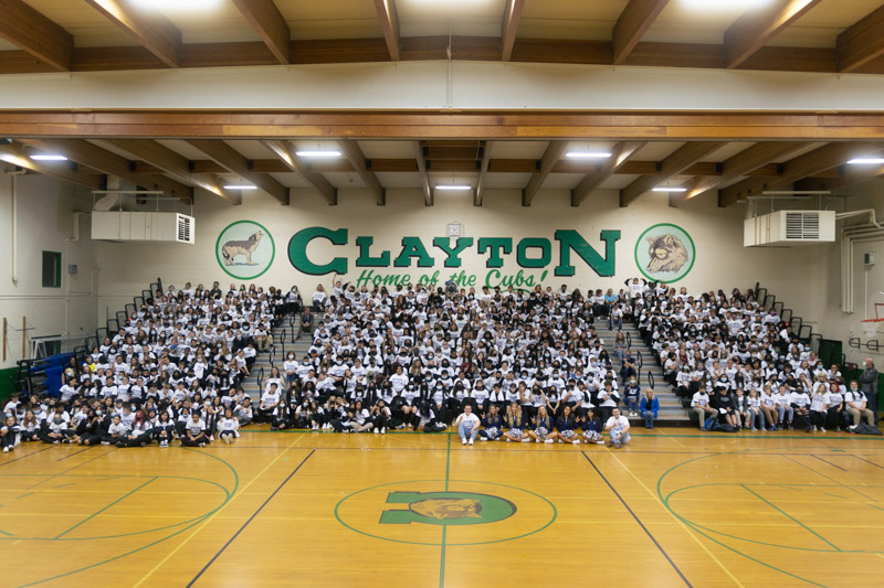 Students sit in the bleachers of the Clayton Middle School gym, wearing white "Future Wolf Pack Student" T-shirts