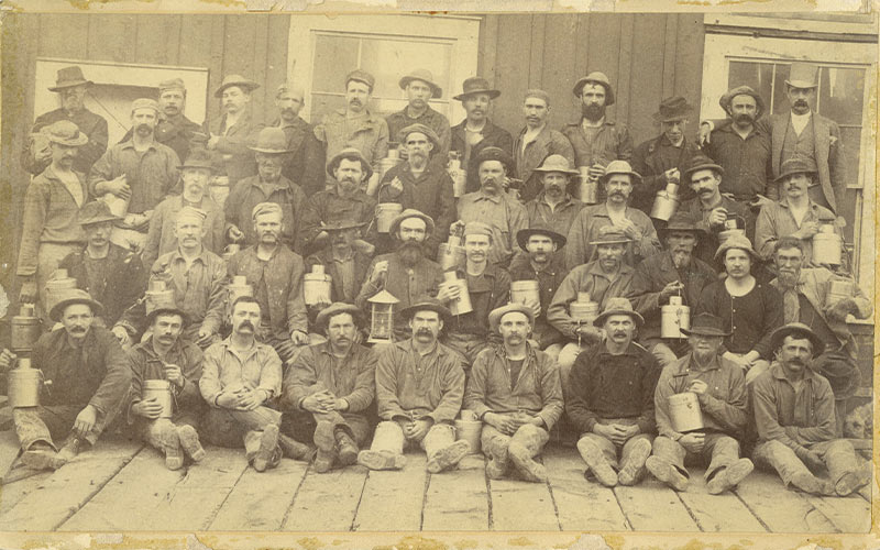 Photographer James Crockwell captures another group of workmen at the Gould and Curry Mine, circa 1888. The shift of miners hold their lunch pails and lanterns before descending.