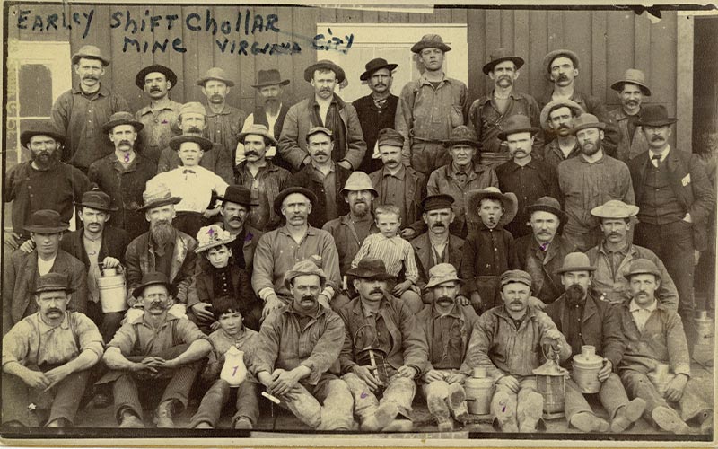 miners at the Chollar Mine in Virginia City, around 1800s. Some children are mixed among the men who hold their lunch pails and a few lanterns