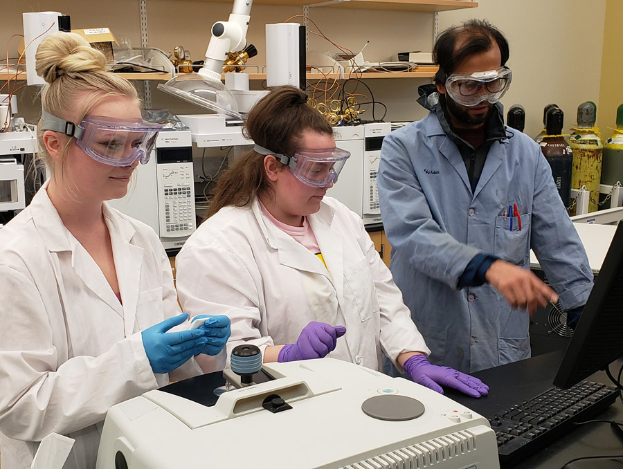 Chemistry Department Graduate Teaching Assistant, Md Azizul Islam, helps Organic Chemistry students Bailey Fasick and Kamryn Montegna analyze a sample of a material they synthesized using an infrared spectrometer.