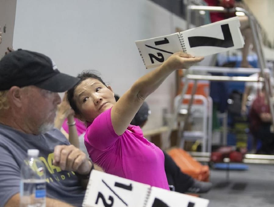 Coach Jian Li You at a diving meet with a score card