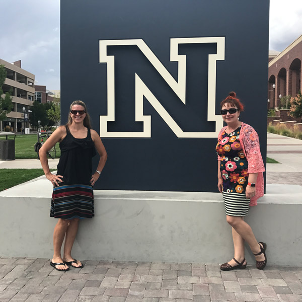 Two women stand on either side of a large sculpture of the University's block N logo.