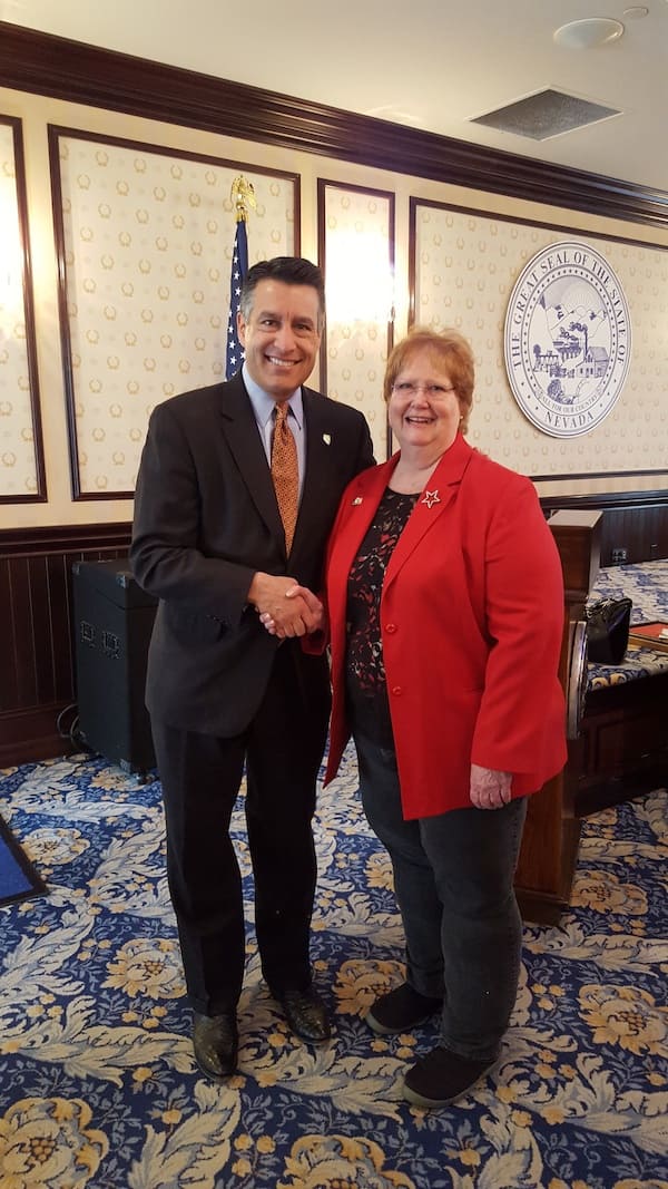 Man in black suit shakes hand with woman on his left in red.