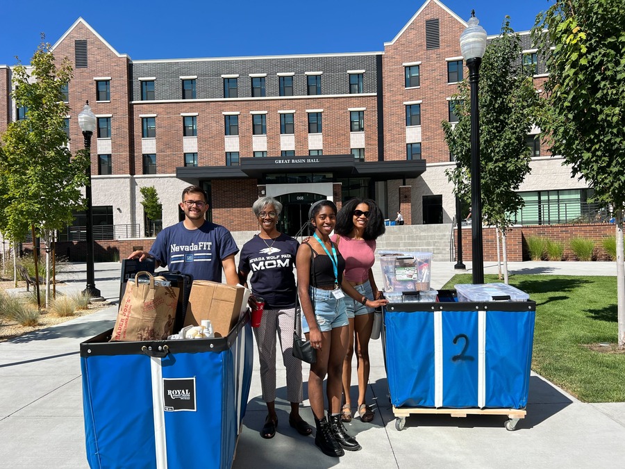 Nevada student Jillian Perry poses with her family and a NevadaFIT volunteer in front of Great Basin Hall with two large carts full of dormitory room items. 