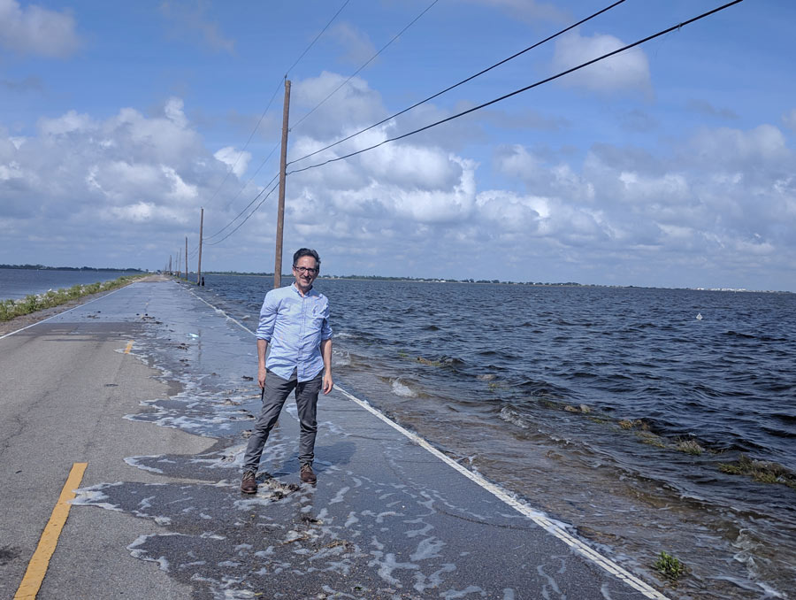 A man stands on a causeway that is flooding.