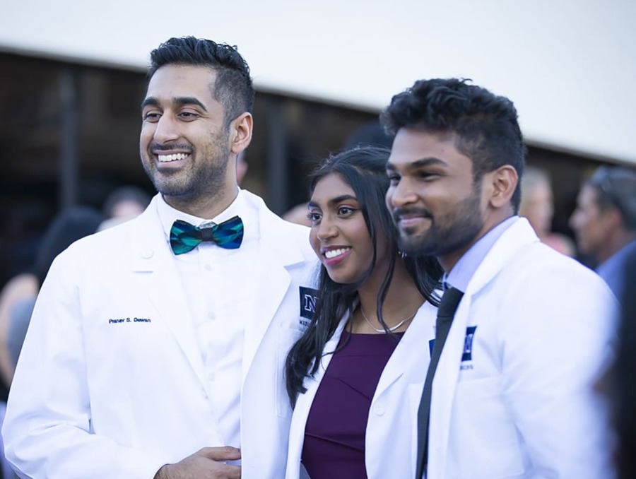 Three students smile for a photo after receiving their white coats