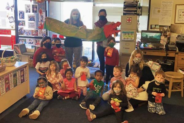 Children learning about holidays in different cultures. Teachers hold a dragon behind the children.