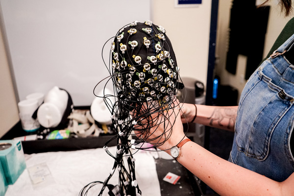 A person holds an electroencephalogram cap. It is black and the electrodes are white dots with black cables running out of them.