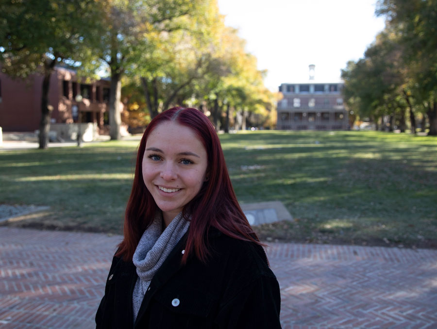 Kimberly Giannantonio smiles, wearing a scarf, as she stands in front of the University Quad.