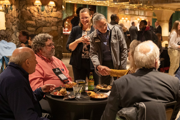 Dean McCall shakes someone's hand as Annie Huhta smiles next to her. There are people at tables with food and drinks around them.