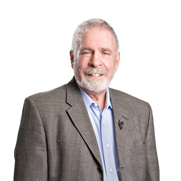 Neil Prenn, wearing a gray suit jacket over a blue button-up shirt, smiles.