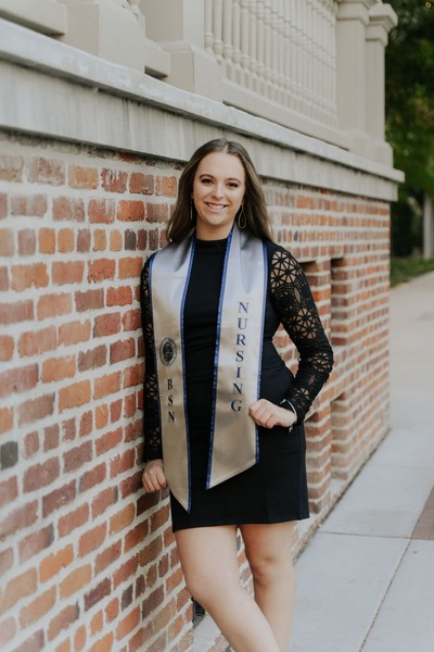 Kaitlynn poses outside in graduation regalia.