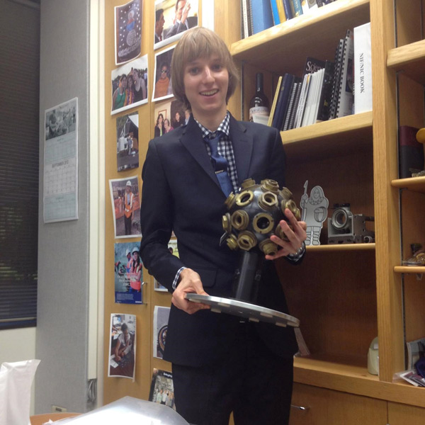 A teenage boy holds a device that looks like a large lollipop made of metal with holes in it.