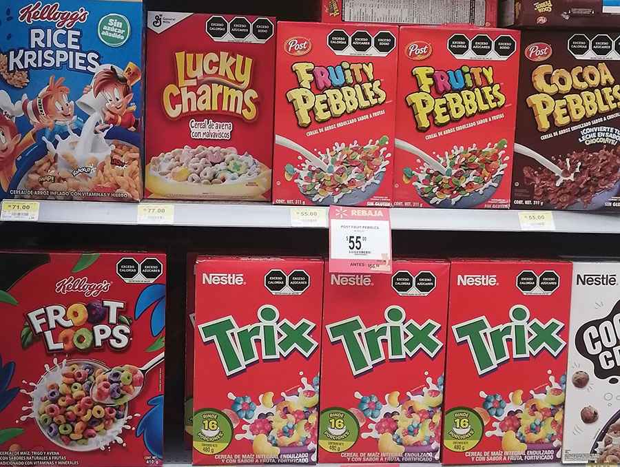 A supermarket shelf with cereal boxes on it with front of package nutrition labels on the top right hand corner