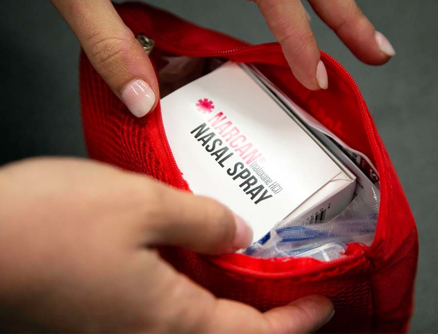 A close-up view of hands opening a small bag with Narcan in it. 
