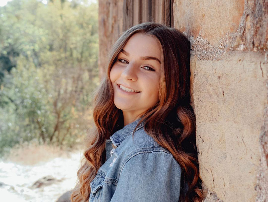 A girl leaning up against a wall outdoors.