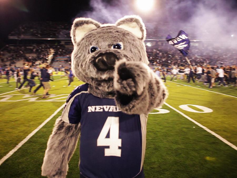 Wolfie the mascot points at the camera while standing on the Nevada football field.