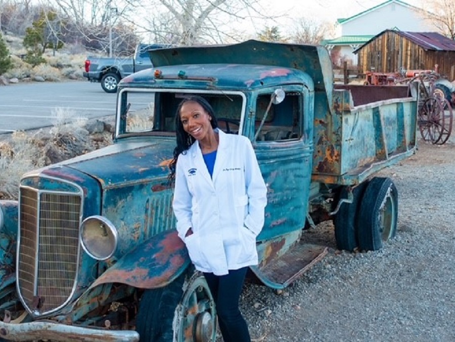 Dr. Bayo Curry-Winchell standing in front of a dilapidated antique truck