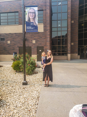 Kyra Morgan holds her daughter and stands next to her banner.