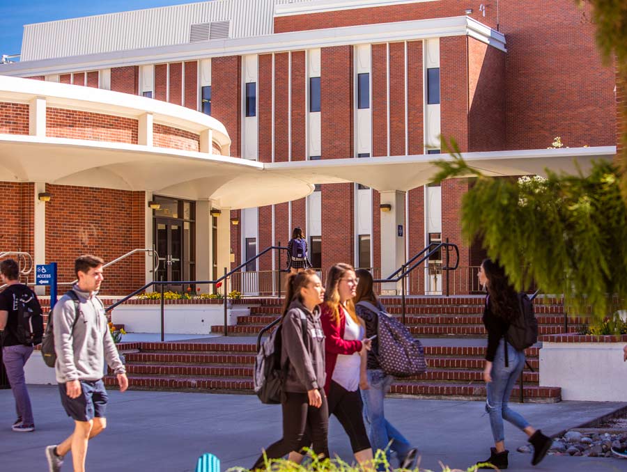 Students walk past the Leifson Physics building on a sunny day.