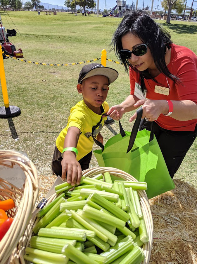 An intern helps a boy choose stalks of celery and place them in his reusable shopping bag.