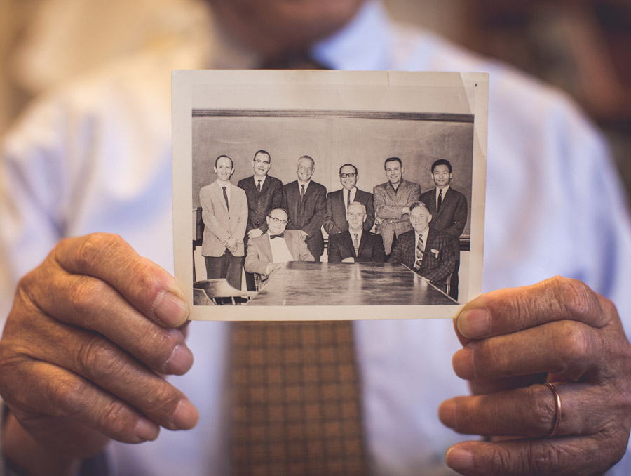 Hyung K. Shin holds a black and white photo in front of him featuring several men around a table.