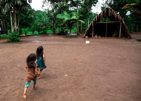 Two young children run barefoot in a community within the Amazon jungle.