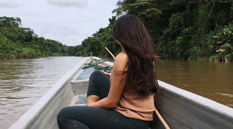 Elizabeth Andi Swanson faces forward in a canoe on a river in the Amazon jungle.