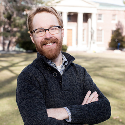 Neil Lareau smiles with his arms crossed on the University quad.