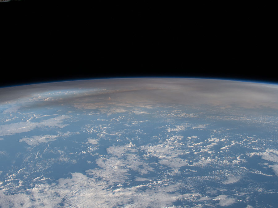 A view of the Earth's horizon from space, with a smoke cloud hanging over part of the atmosphere.
