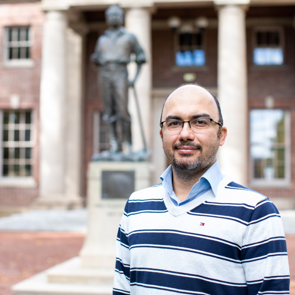 Ehsan Vahidi smiles wearing a striped shirt in the foreground, with the Mackay Statue in the background.